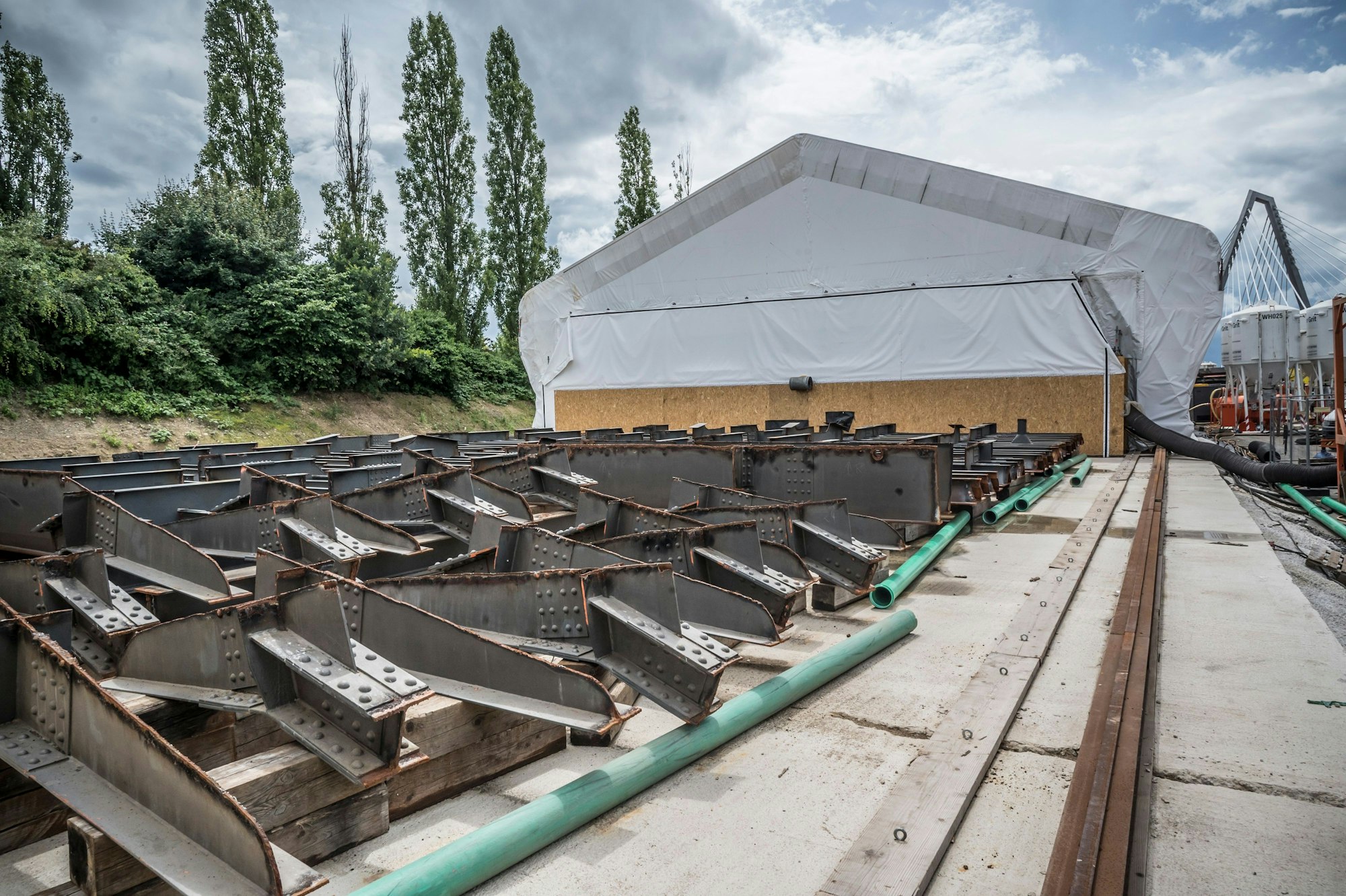 Stahlteile, die noch sandgestrahlt werden müssen, liegen vor einem Bauzelt.