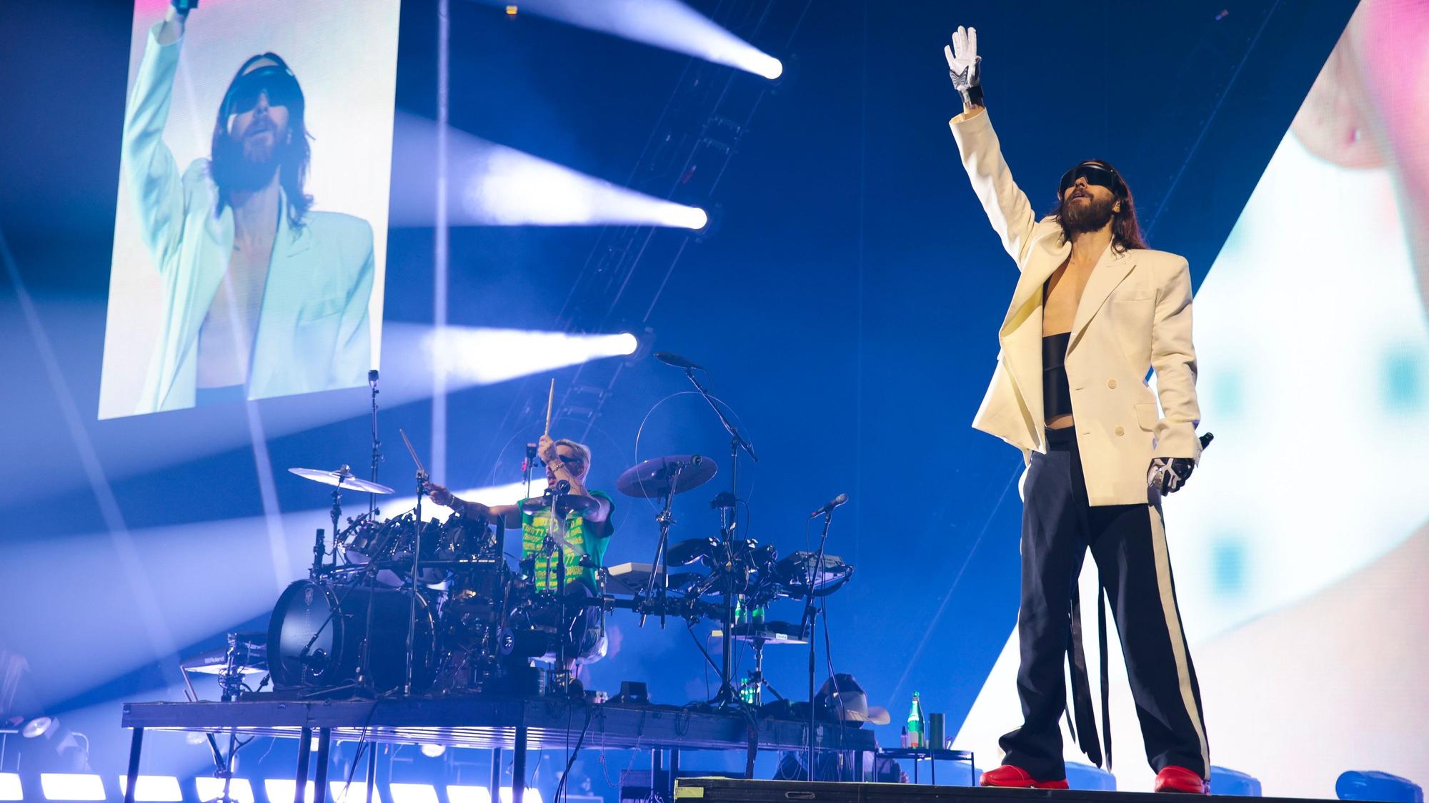 Leadsänger Jared Leto steht im Vordergrund, sein Bruder und Schlagzeuger Shannon sitzt links von ihm an seinem Gerät. Im Hintergrund zeigen Bildschirme Jared in Großaufnahme und das Musikvideo des Songs.