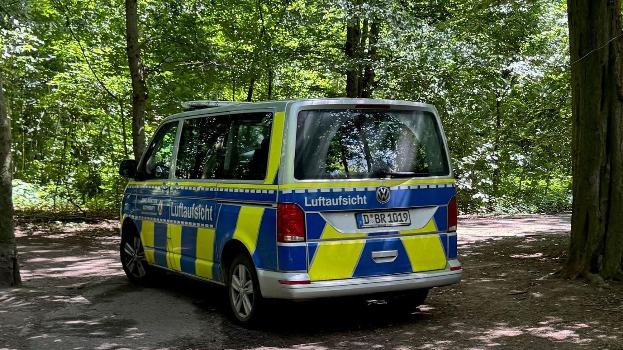 Ein gelb-blauer Polizeiwagen mit der Aufschrift „Luftaufsicht“ steht im Stadtwald.
