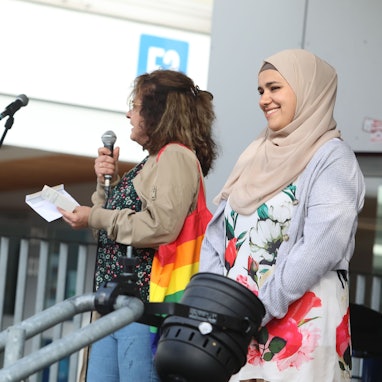 Drei Frauen stehen auf einer Bühne, eine hält ein Mikrofon in der Hand.
