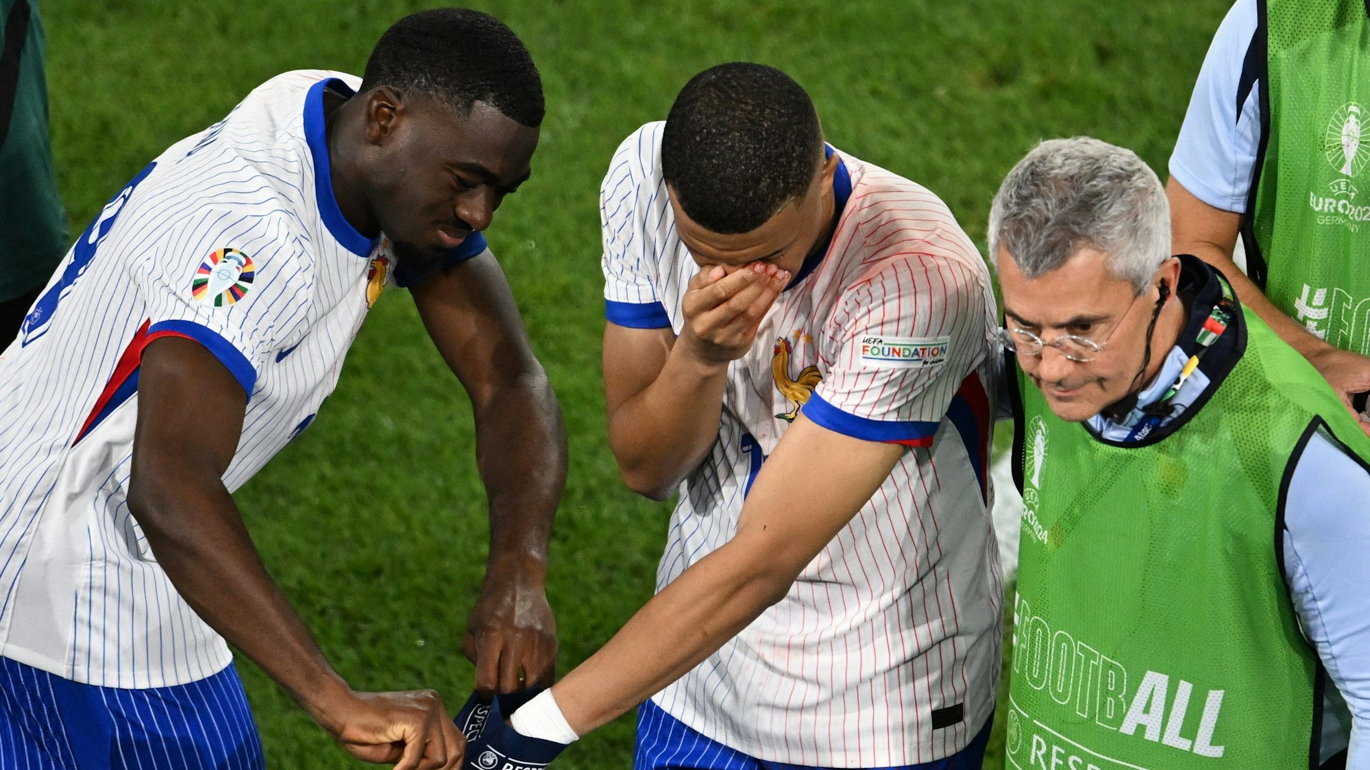 Frankreichs Superstar Kylian Mbappé (M) hält sich bei seiner Auswechslung die blutige Nase und bekommt Hilfe von Teamkollege Youssouf Fofana.