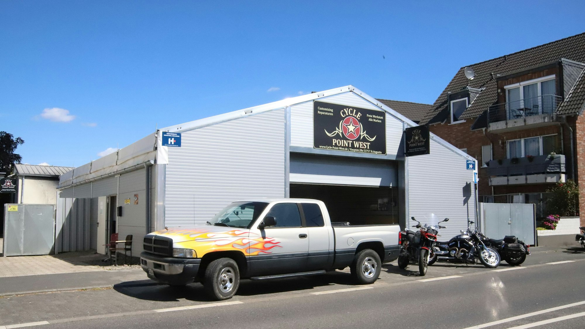 In einem Leichtbauzelt ist der Motorradladen untergebracht. Davor stehen ein Pick-Up und mehrere Motorräder.