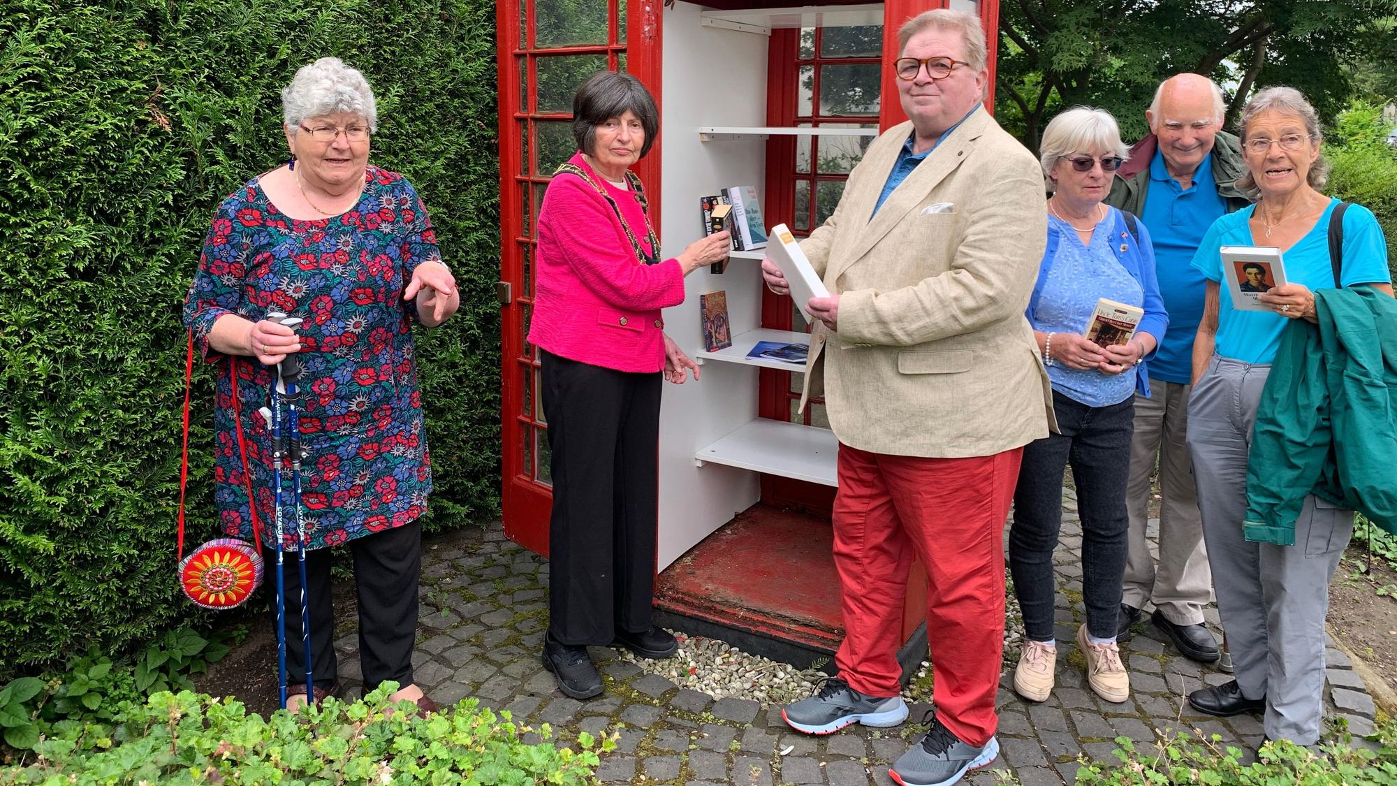 Mehrere Menschen stehen an einem öffentlichen Bücherschrank.