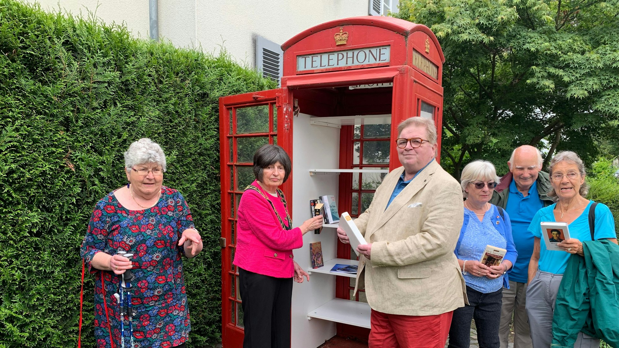 Personen legen Bücher in einen Bücherschrank.
