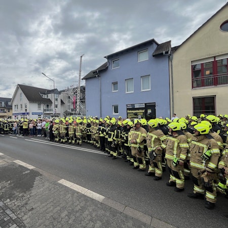Viele Menschen, darunter hunderte Feuerwehrleute stehen auf einer Straße.