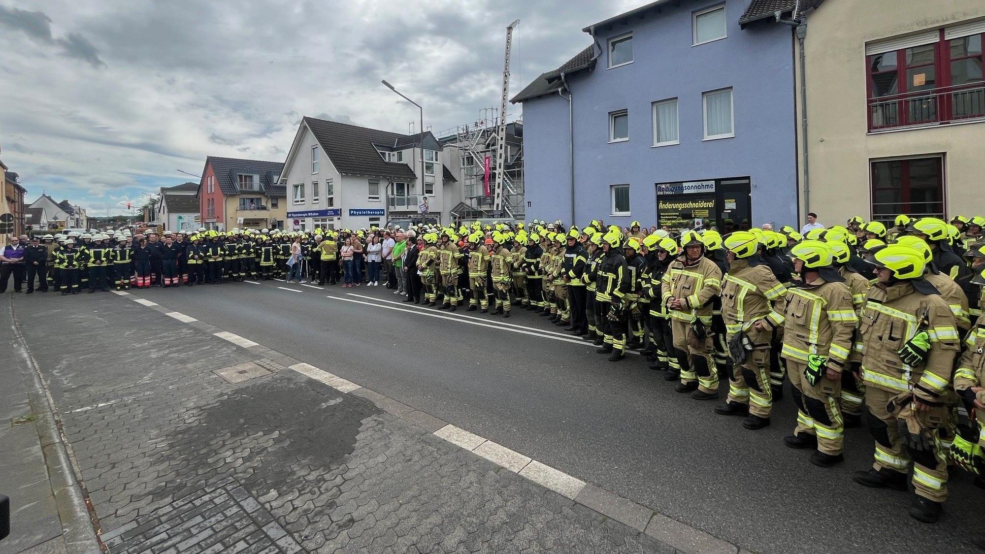 Viele Menschen, darunter hunderte Feuerwehrleute stehen auf einer Straße.