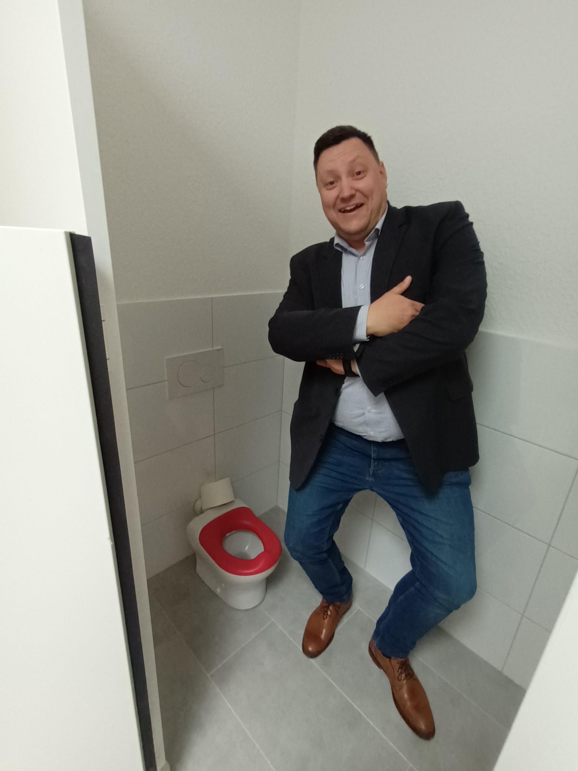 Toilette mit roter Brille für Kleinkinder, daneben steht ein großer Mann.