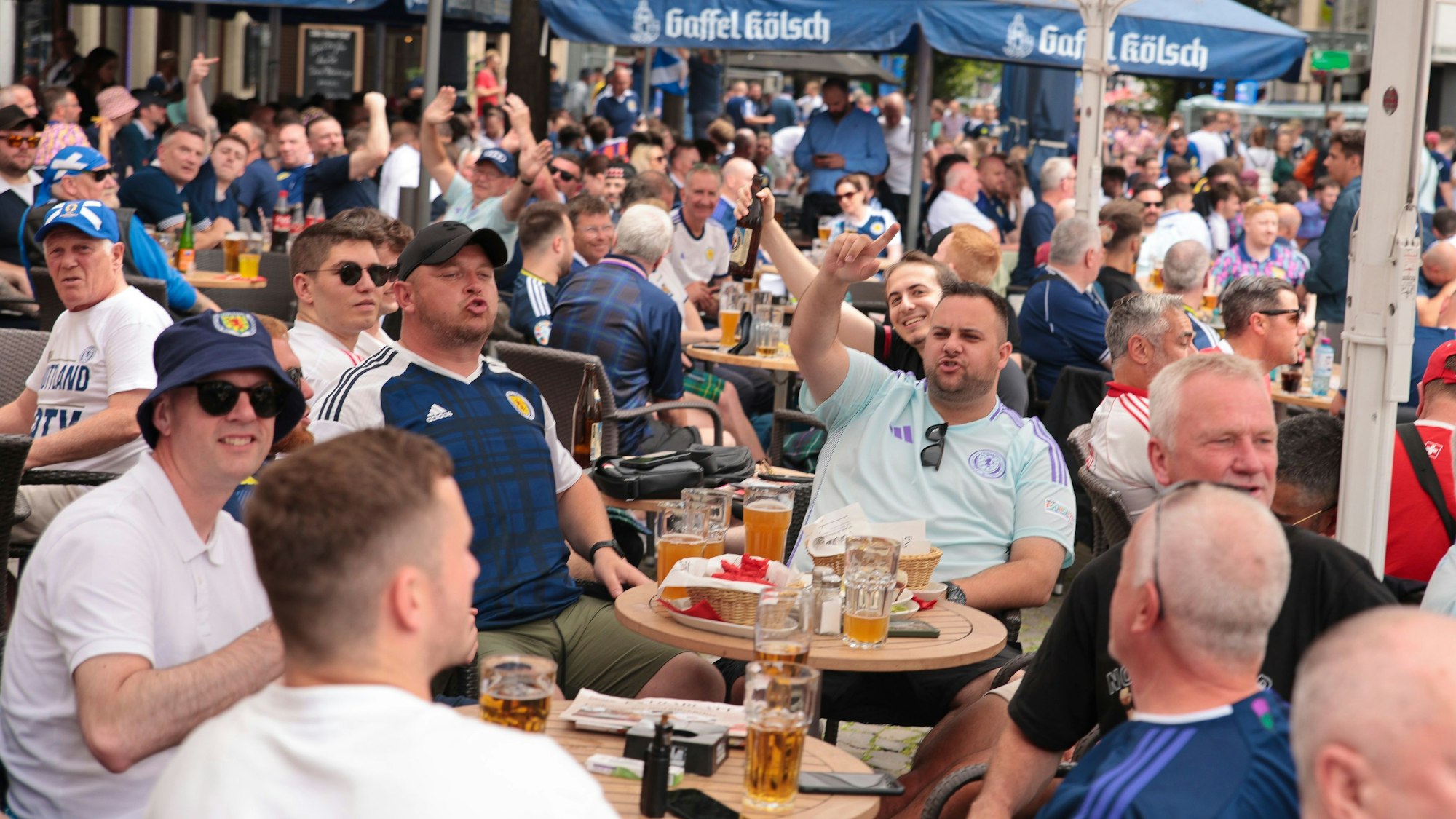 Zu sehen sind schottische Fußballfans, die an Tischen Bier trinken.