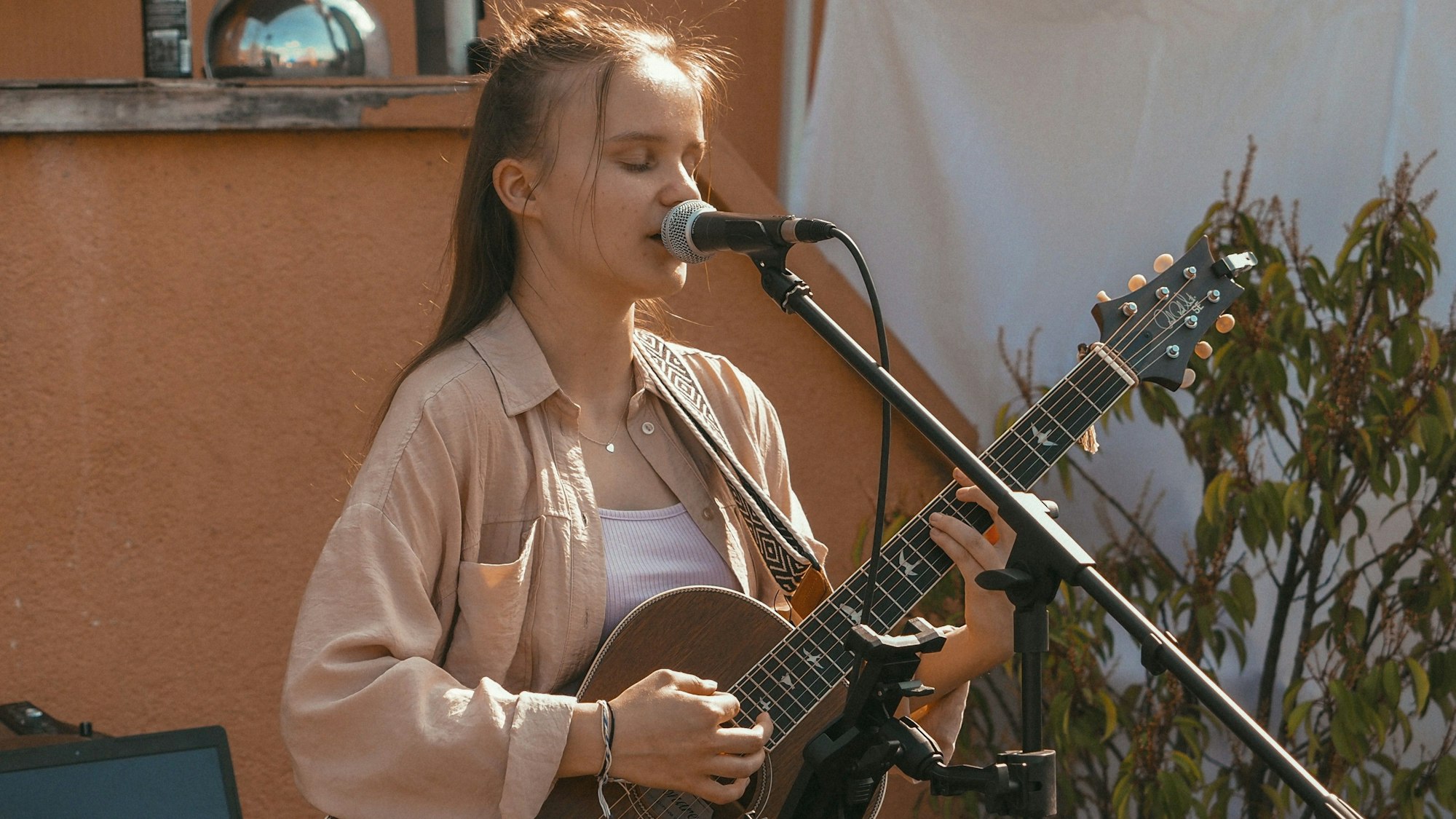 Kira Grohs steht mit einer Gitarre in der Hand vor einem Mikrofon und singt.