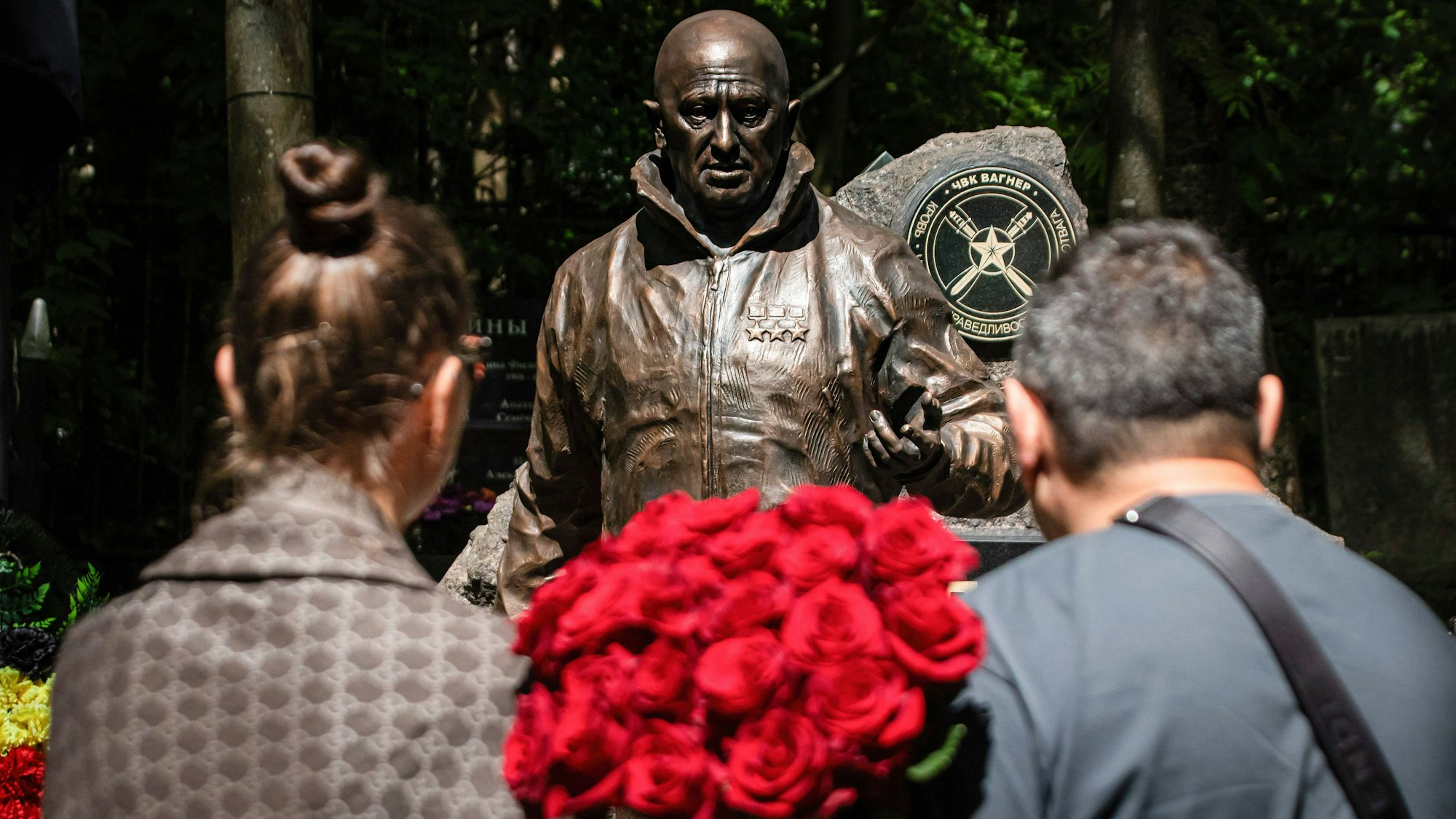 Menschen stehen mit einem Rosenstrauß in der Nähe einer Skulptur des russischen Söldnerführers Jewgeni Prigoschin, die auf seinem Grab in St. Petersburg aufgestellt wurde.