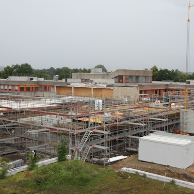 Blick auf eine Großbaustelle, im Hintergrund ein Schulzentrum