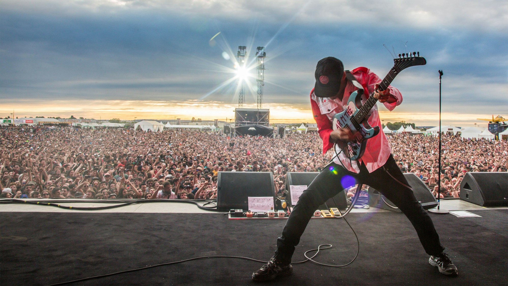 Tom Morello spielt auf einem Festival, hinter ihm kann man eine Menge aus Zehntausenden von Zuhörern erkennen.