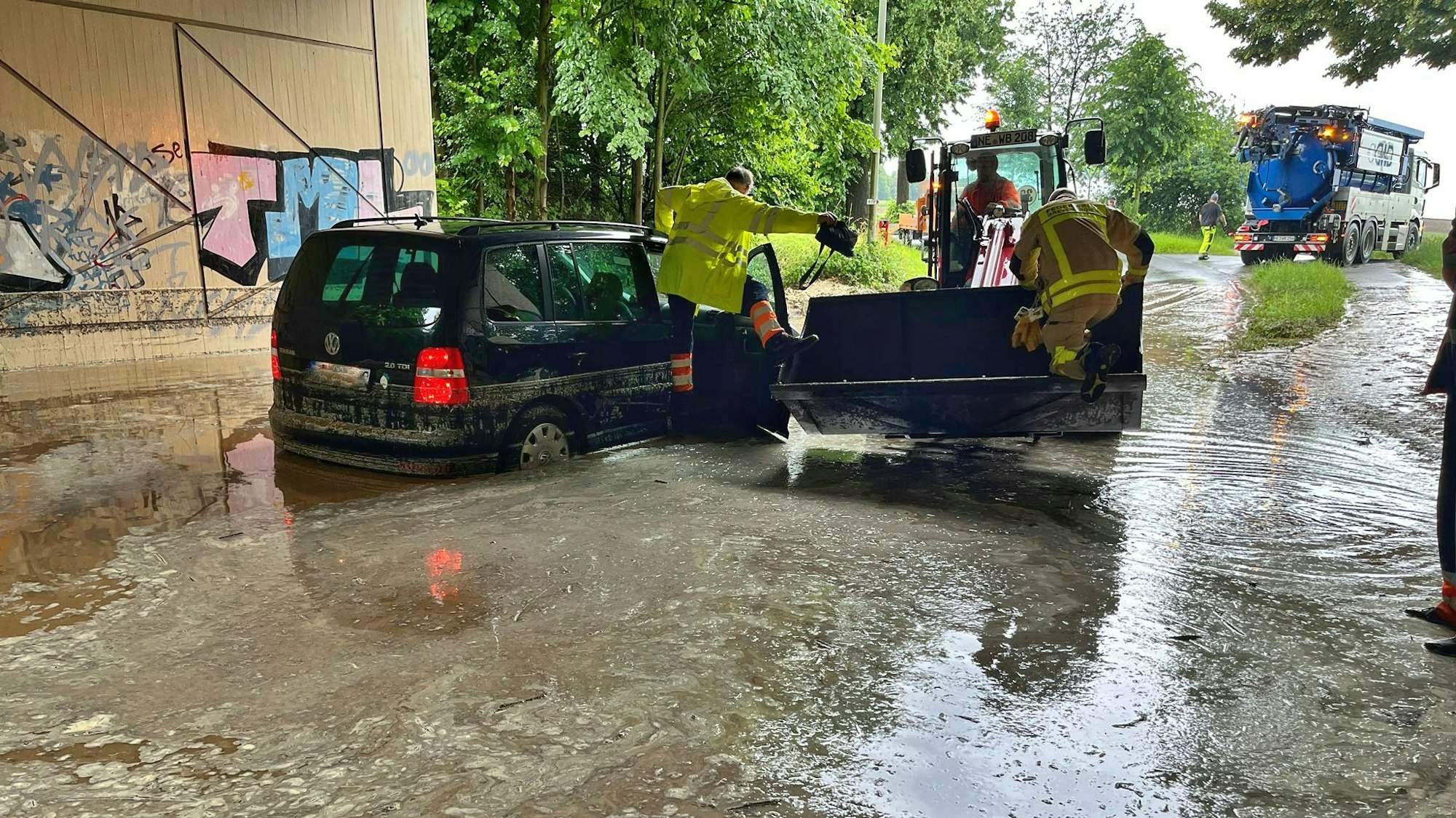 Einsatzkräfte der Feuerwehr auf einem Fahrzeug, das in einer Unterführung im Wasser steht.
