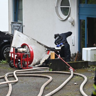 Ein Polizist steht vor der Eingangstür zu einem Mehrfamilienhaus. Zwei THW-Kräfte schauen ihm zu.