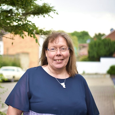 Kerstin Roscher steht auf einem Bürgersteig in Zülpich, links von ihr ist ein Baum zu erkennen.