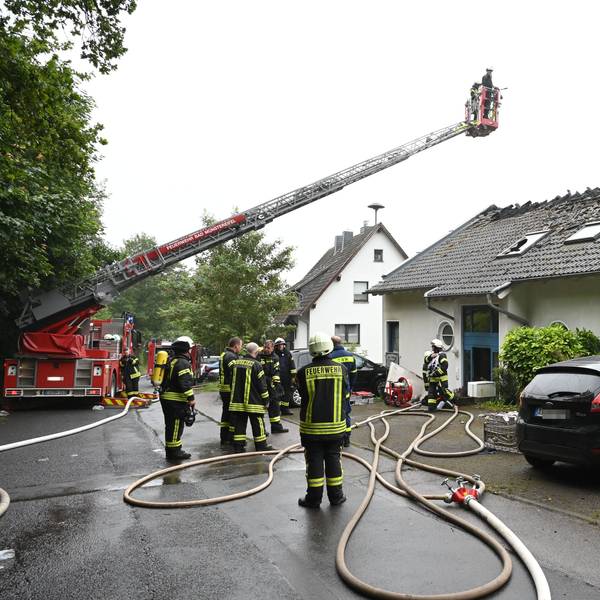Zahlreiche Feuerwehrleute stehen vor einem Haus in Bad Münstereifel-Holzem. Eine Drehleiter ist ausgefahren, das Dach massiv beschädigt. Das Bild stammt vom Juni 2024.