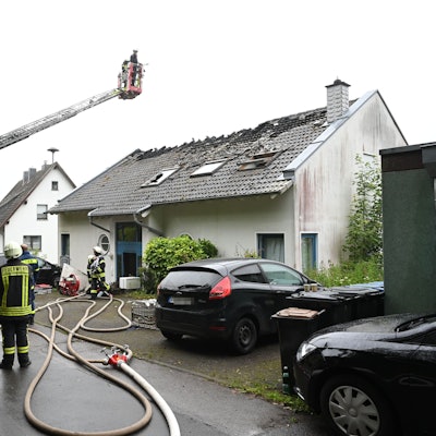 Die Feuerwehr hat über dem Haus eine Drehleiter ausgefahren, Einsatzkräfte stehen auf der Straße.