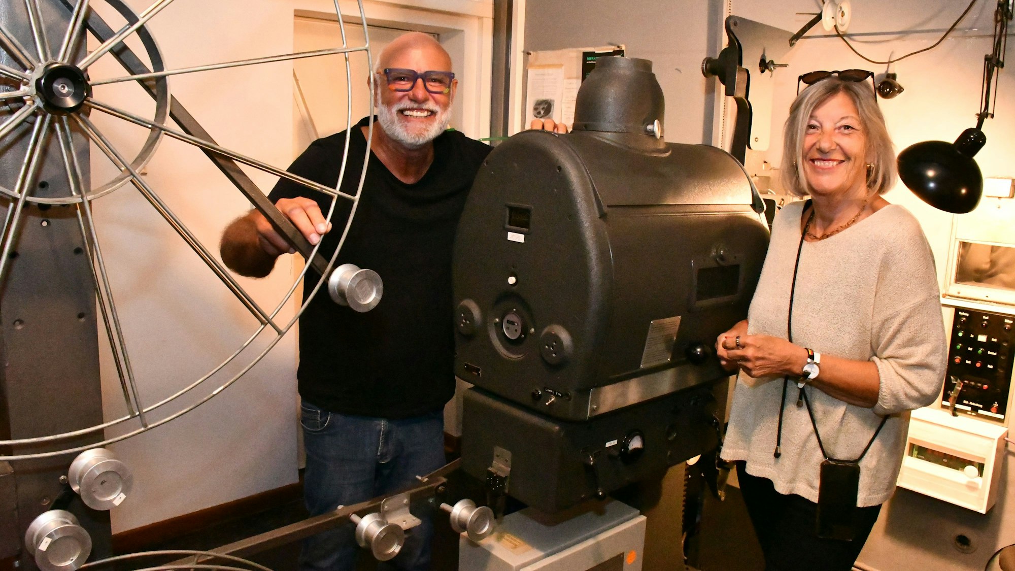 Die Vorsitzenden des Kinoklubs im Vorführraum des Berli-Kinos vor einem alten Projektor mit großer Filmspule.