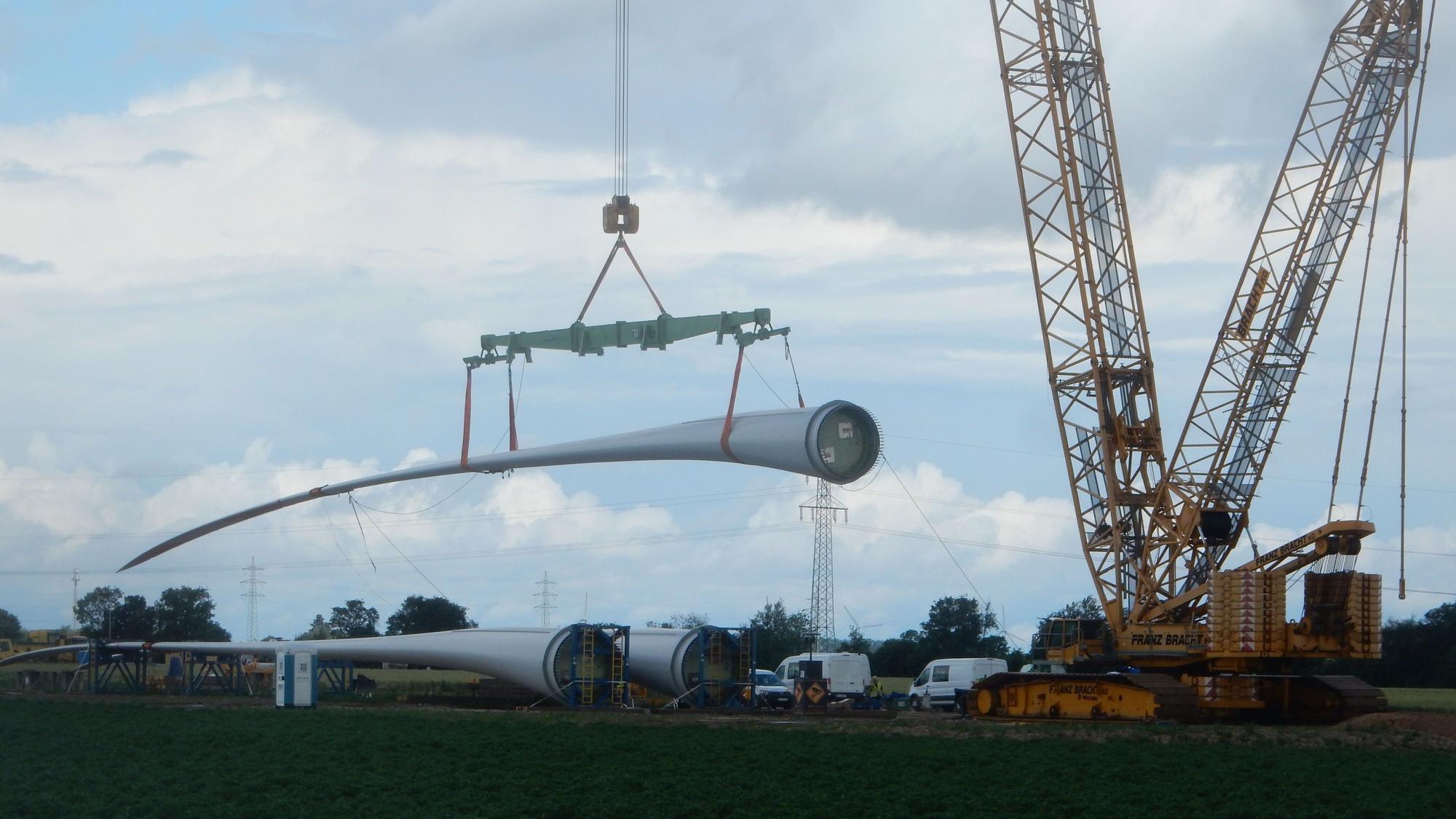 Ein Rotorblatt einer Windkraftanlage wird von einem Kran angehoben.