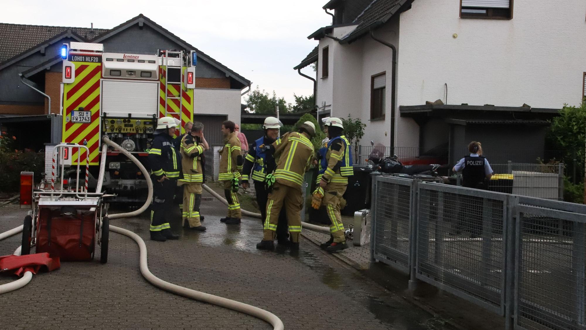 Die Freiwillige Feuerwehr Lohmar steht mit einem Löschfahrzeug vor einem Haus.