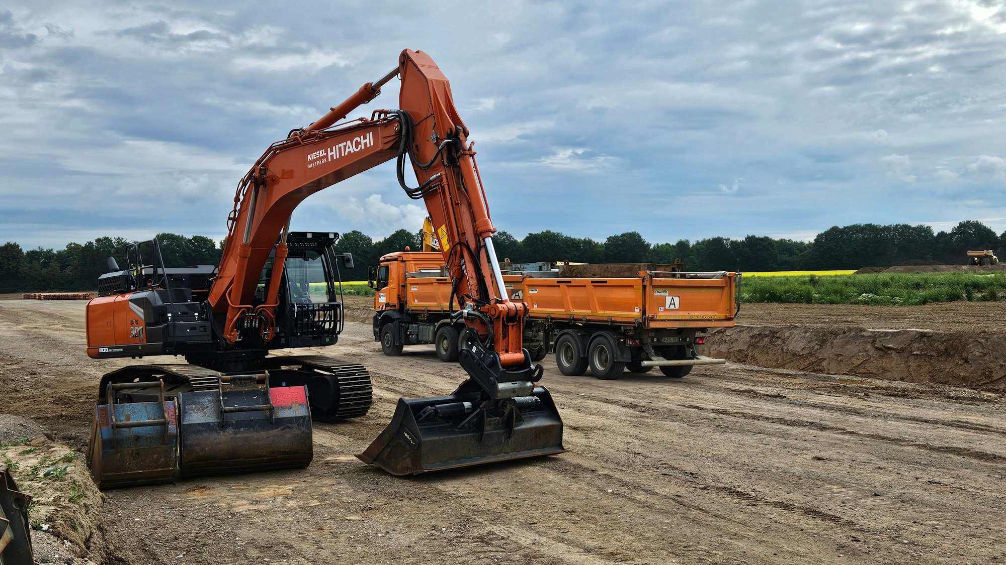 Ein Bagger und ein Bau-Lkw sind auf einem Bau-Abschnitt zu sehen.