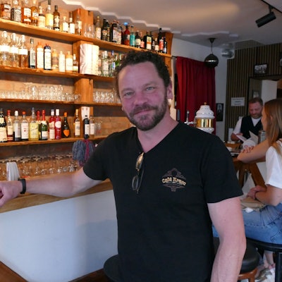 Ein Mann in schwarzem T-Shirt sitzt vor seiner Theke.