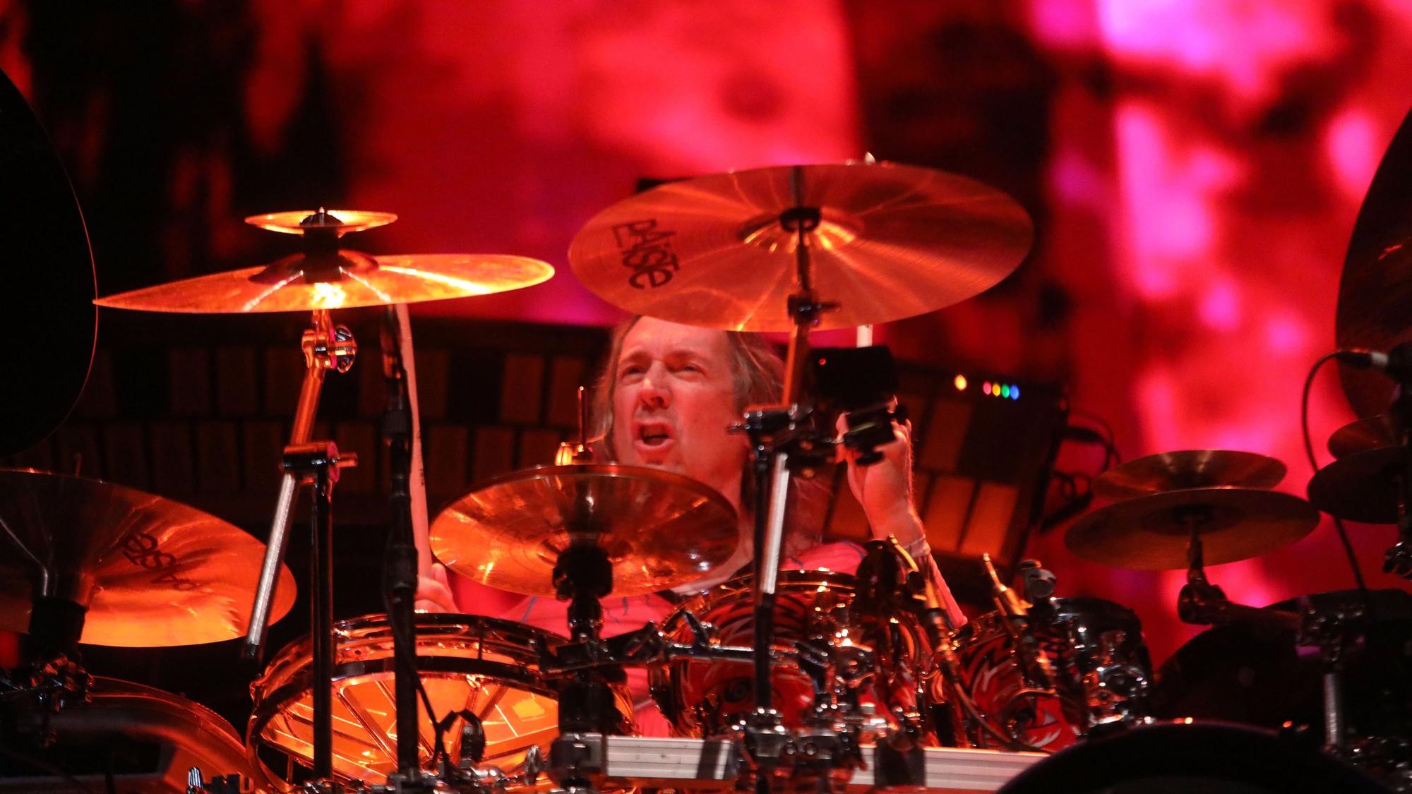Der Schlagzeuger Danny Carey von Tool sitzt an seinem Arbeitsgerät. Im Hintergrund sieht man schemenhaft die Visualisierung der Musik der Band.