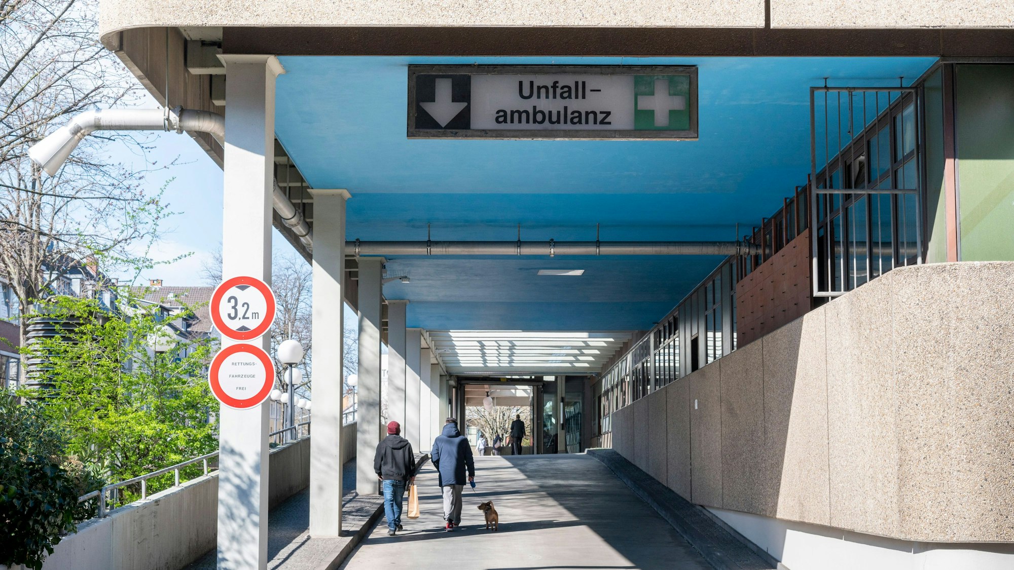 Zu sehen ist die Krankenwagenanfahrt eines Krankenhauses und einige Fußgänger.