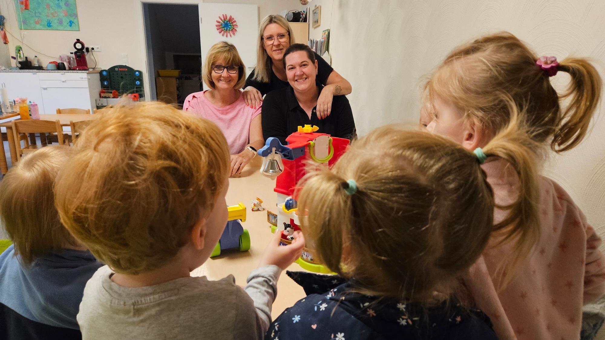Drei Frauen sitzen an einem Tisch mit einer Gruppe von Kleinkindern.