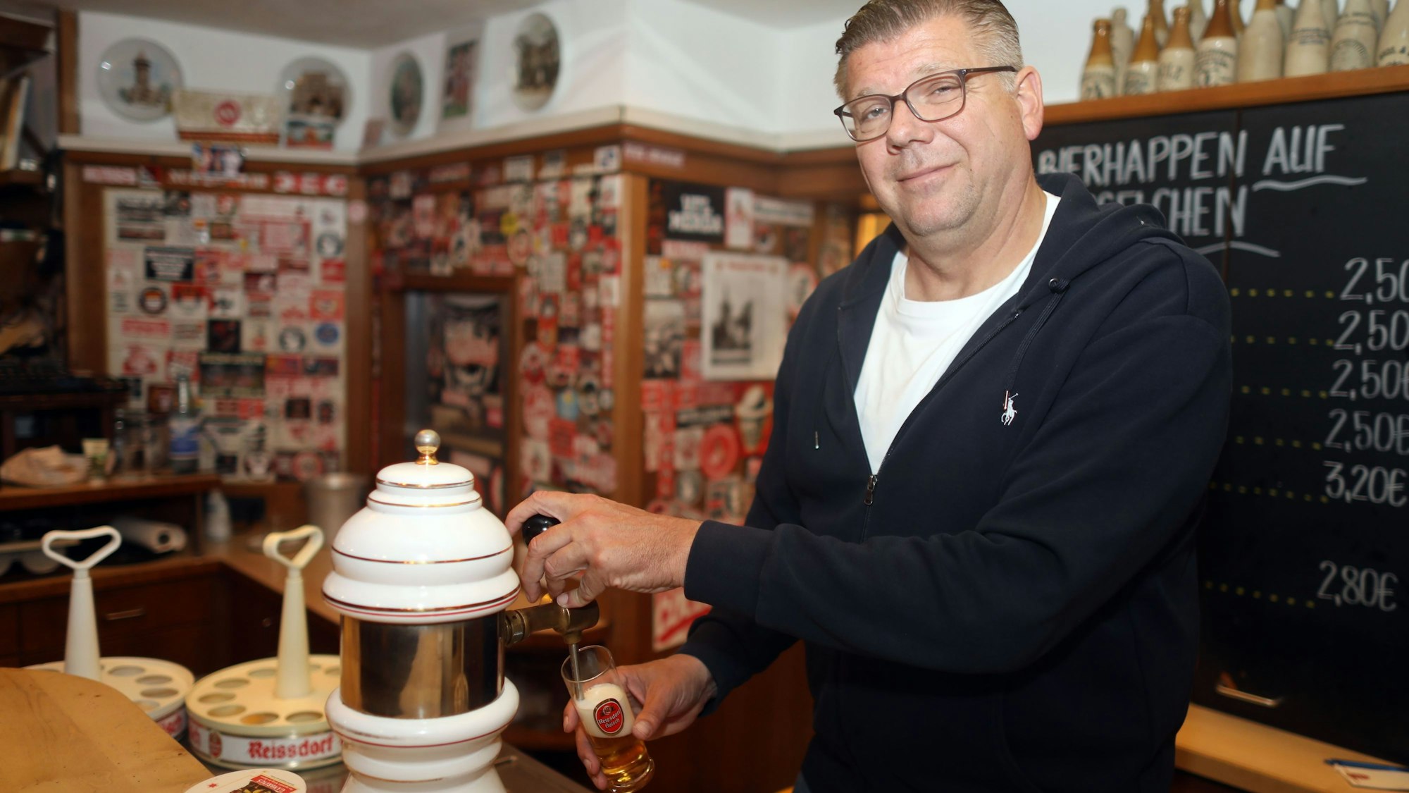 Mann mittleren Alters an einer Theke, der ein Kölsch zapft