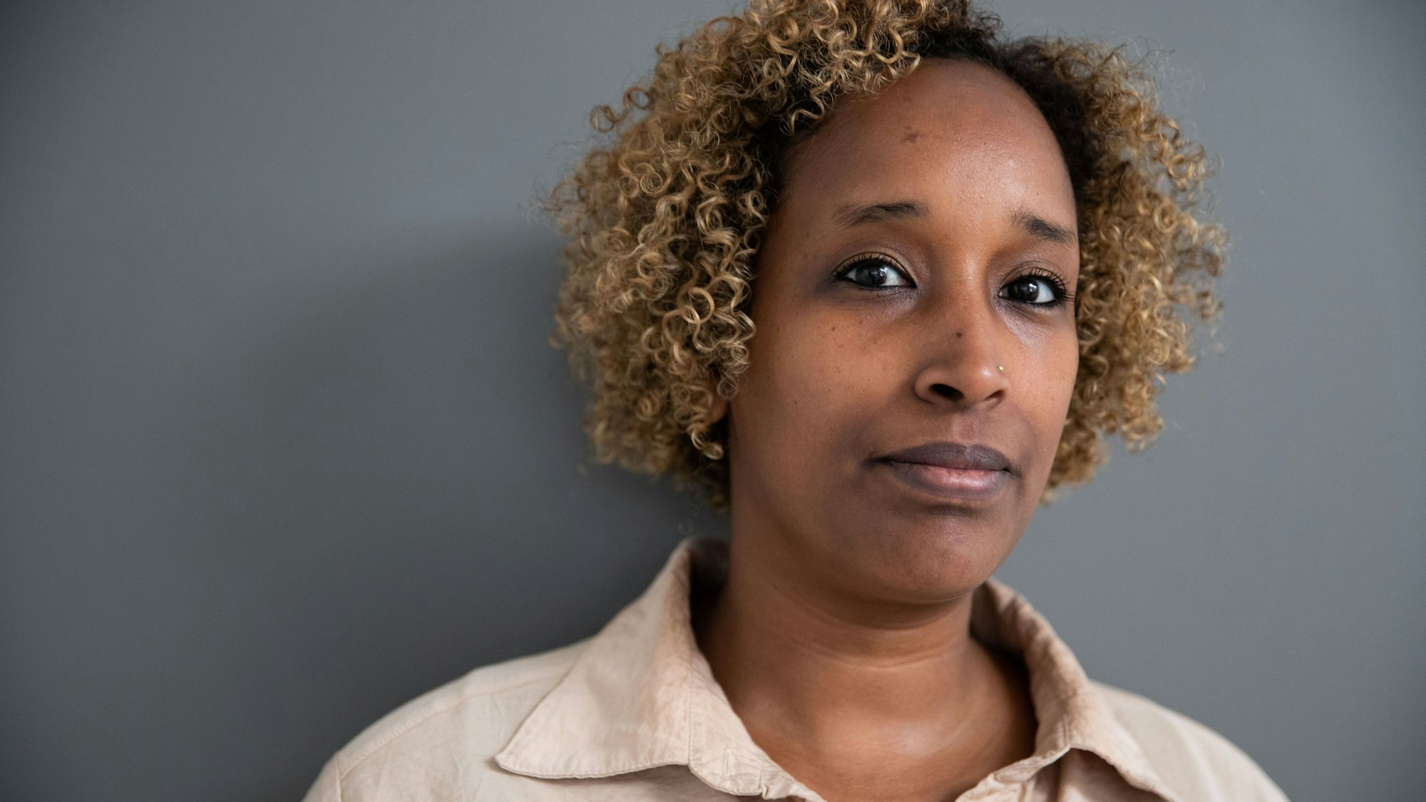 Zu sehen ist die Autorin Lubi Barre. Sie hat lockige, hellbraune Haare und trägt ein beiges Hemd.