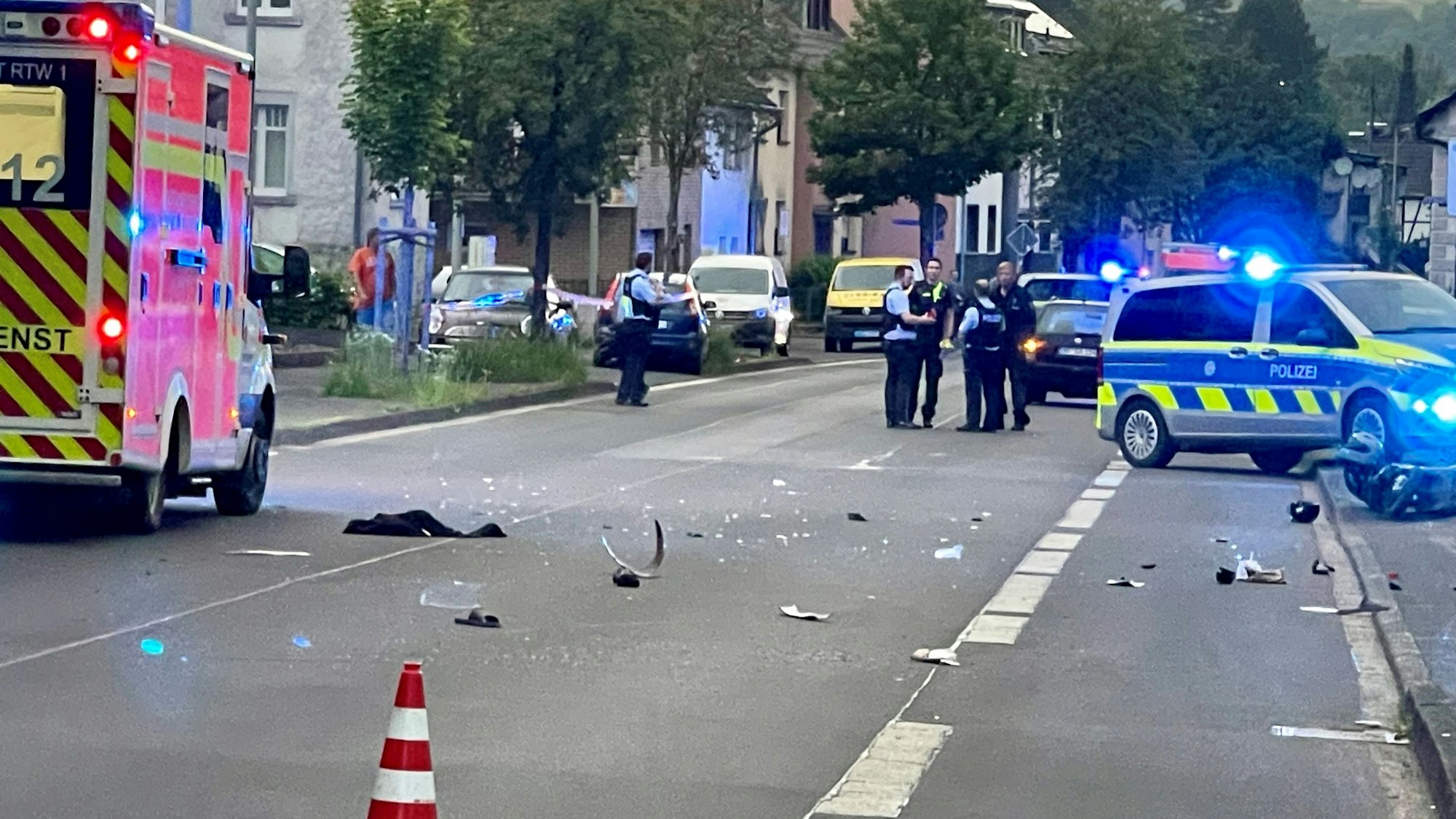 Ein Rettungswagen und ein Polizeifahrzeug sowie mehrere Polizeibeamte stehen auf der Asbacher Straße in Eirtorf, Trümmerteile liegen auf dem Asphalt.