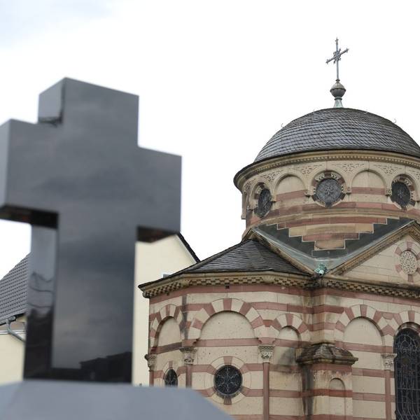 Im Vordergrund ein Kreuz, im Hintergrund ein Gebäude mit einer Kuppel.