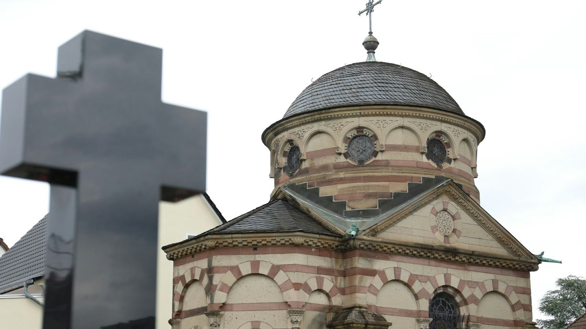 Im Vordergrund ein Kreuz, im Hintergrund ein Gebäude mit einer Kuppel.