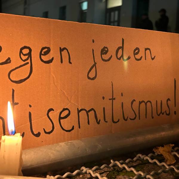 Eine brennende Kerze steht vor einem Schild mit der Aufschrift „Gegen jeden Antisemitismus“
