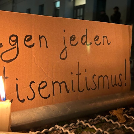 Eine brennende Kerze steht vor einem Schild mit der Aufschrift „Gegen jeden Antisemitismus“
