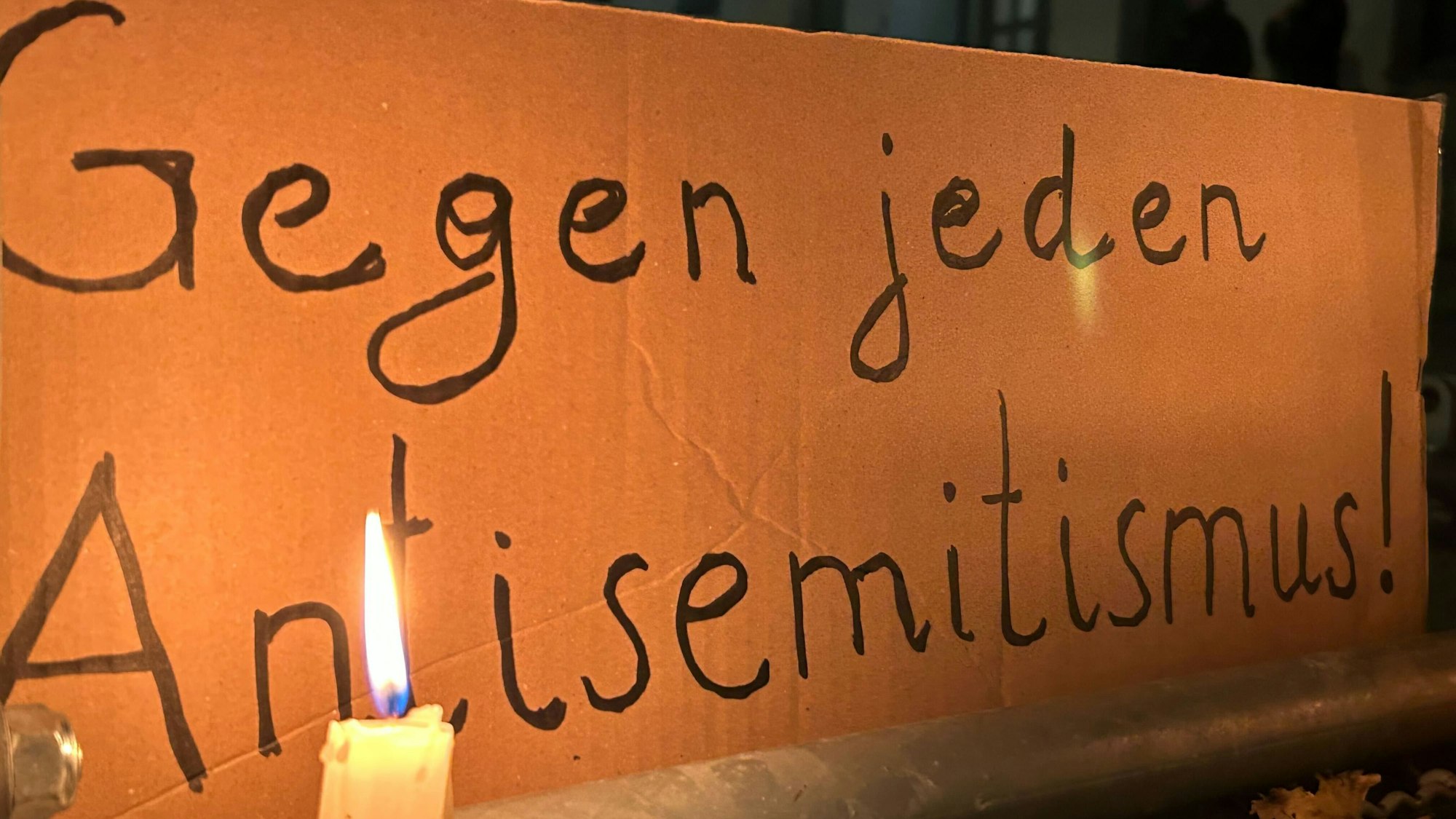 Eine brennende Kerze steht vor einem Schild mit der Aufschrift „Gegen jeden Antisemitismus“