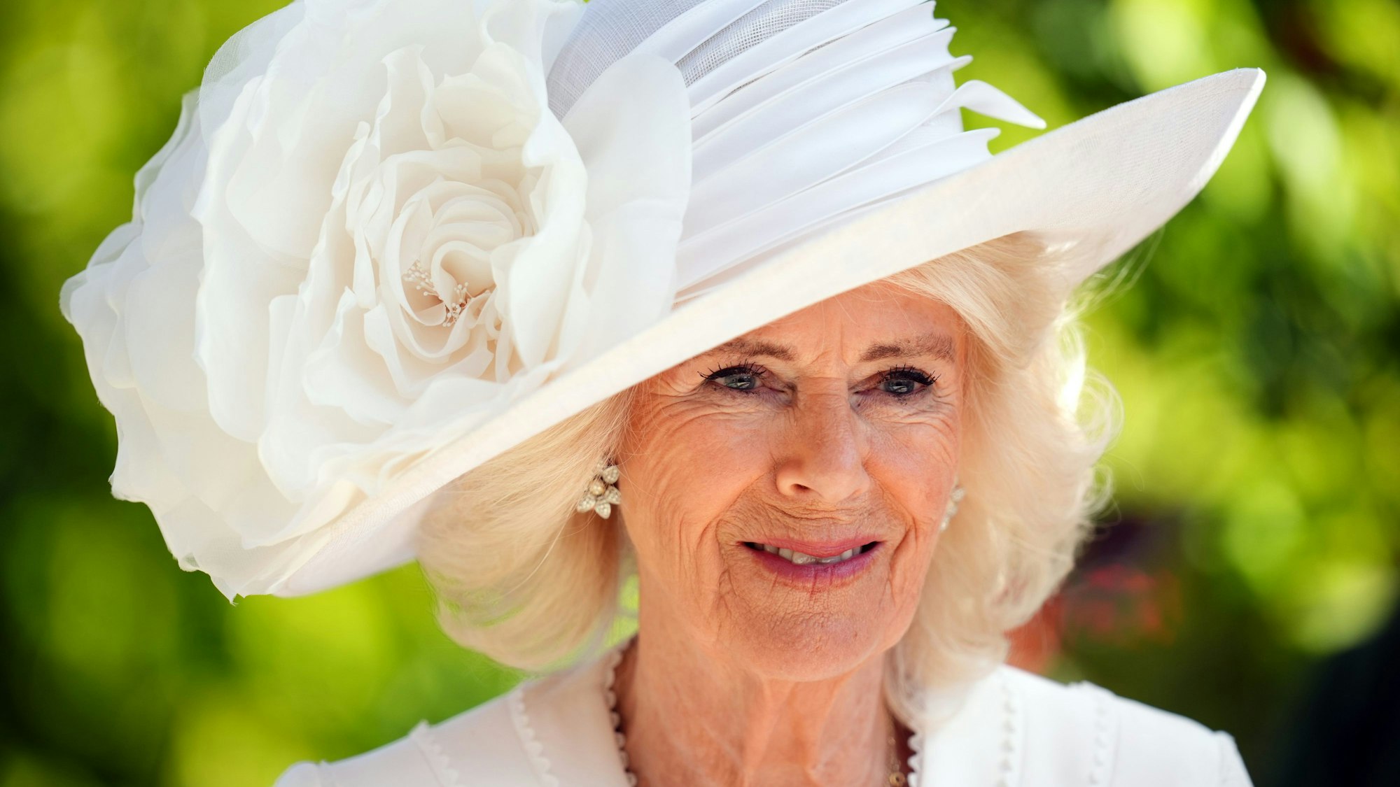 Königin Camilla trägt am dritten Tag von Royal Ascot auf der Pferderennbahn einen weißen Hut mit einer großen weißen Blüte.