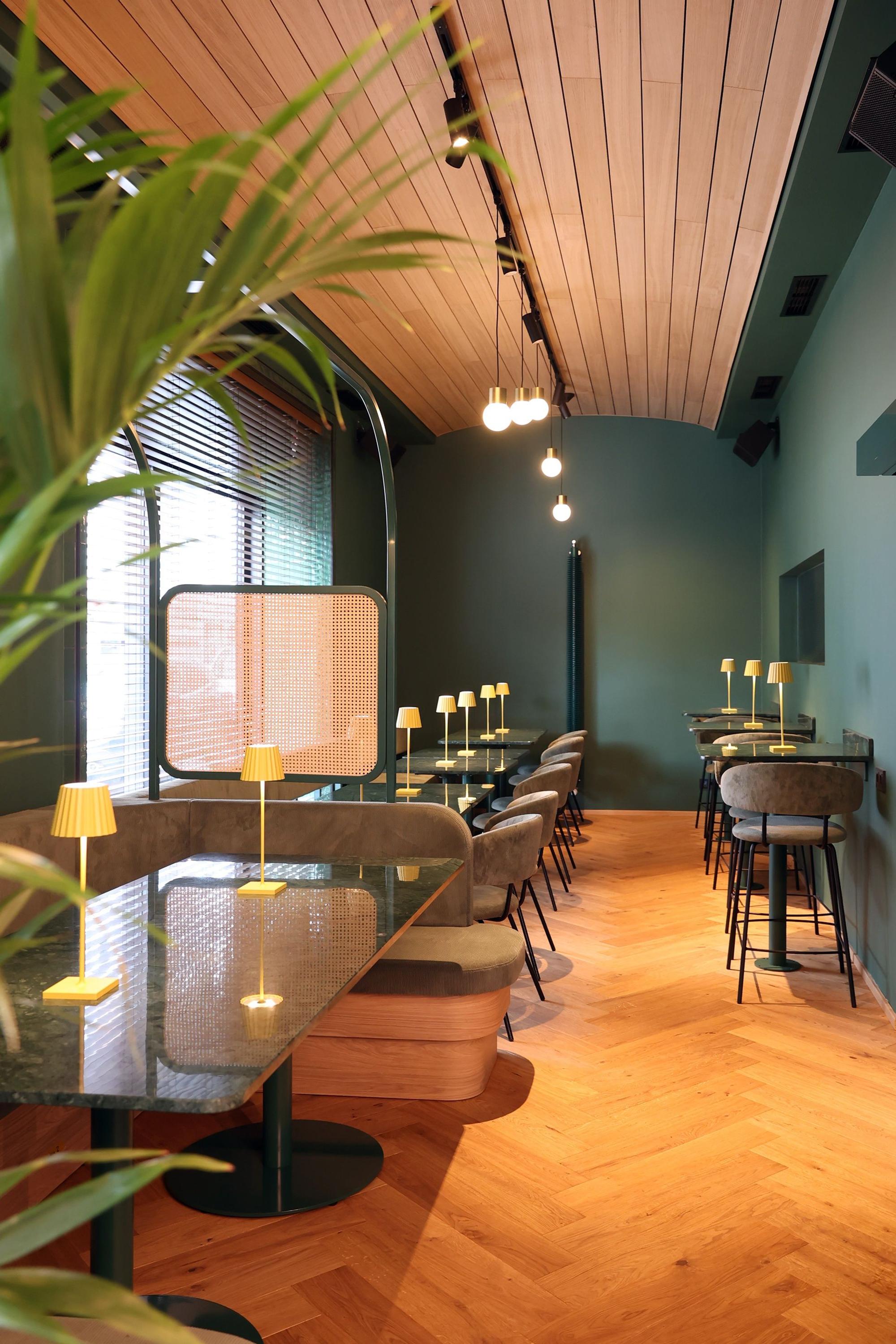 Blick in den Innenraum des Restaurants mit grünen Wänden, holzvertäfelter Decke und Holzboden.