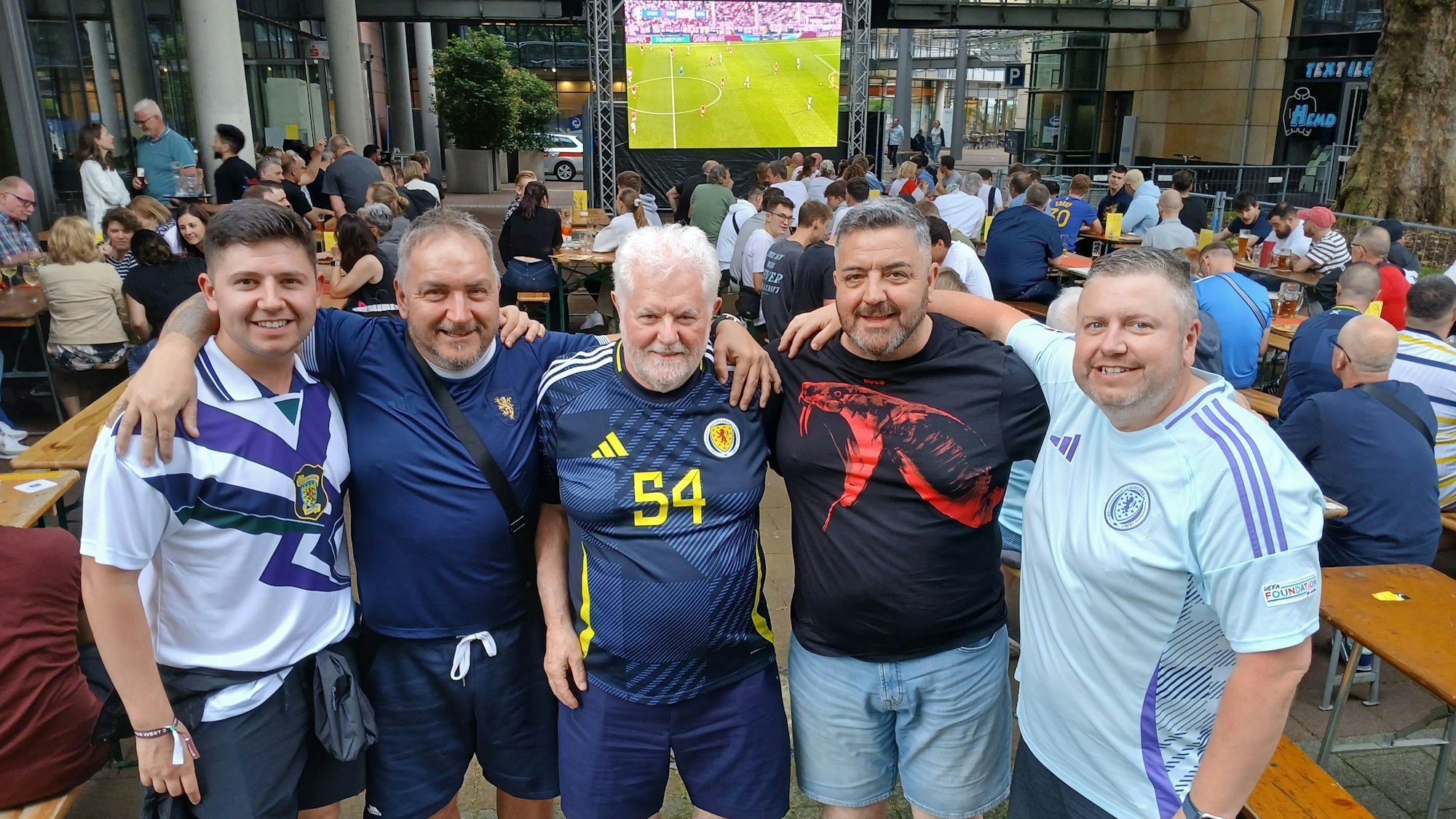 Fünf Männer in einem Biergarten vor einem Public-Viewing-Bildschirm.