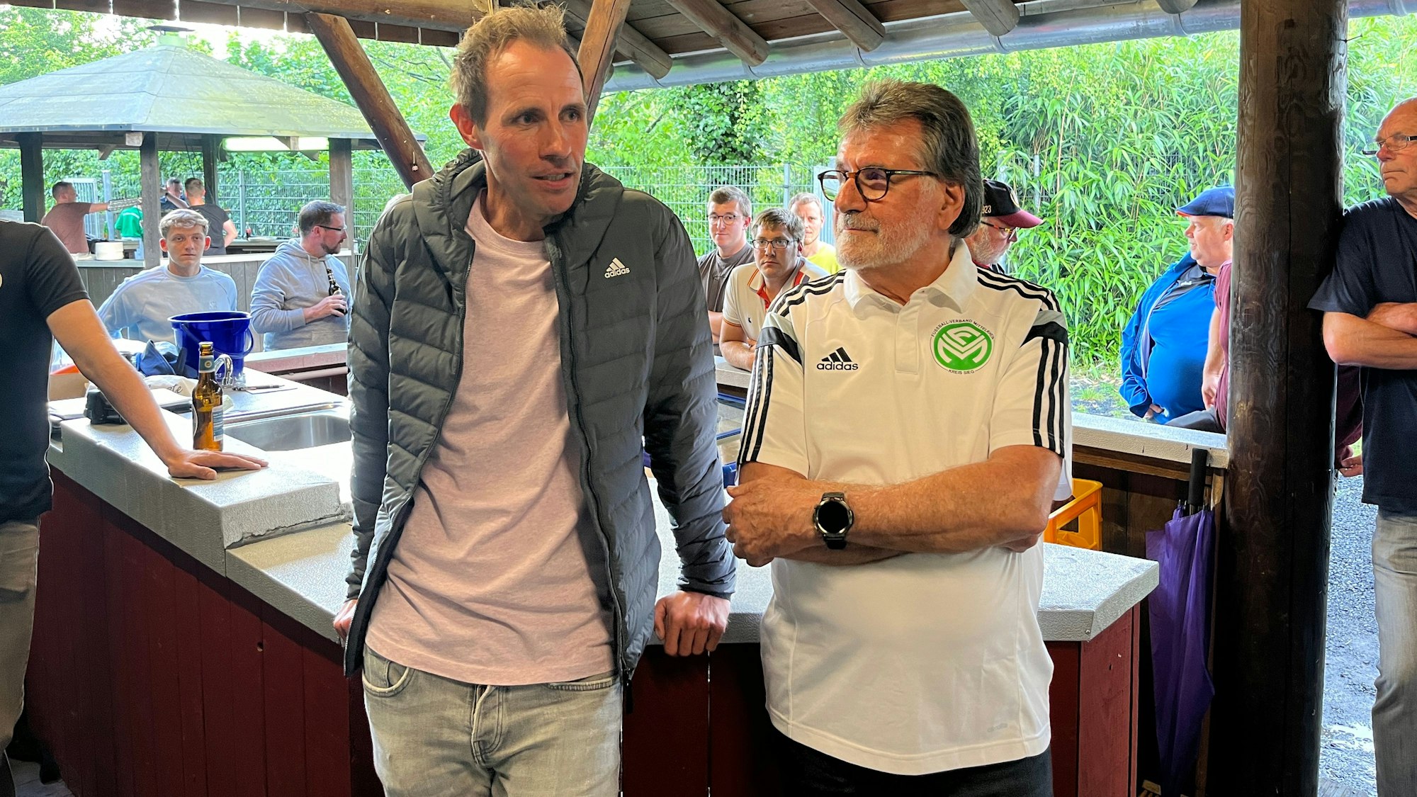 Bundesliga-Referee Sascha Stegemann und der Kreis-Schiedsrichter-Vorsitzende Günter Gertmann stehen in einer Grillhütte am Tresen.