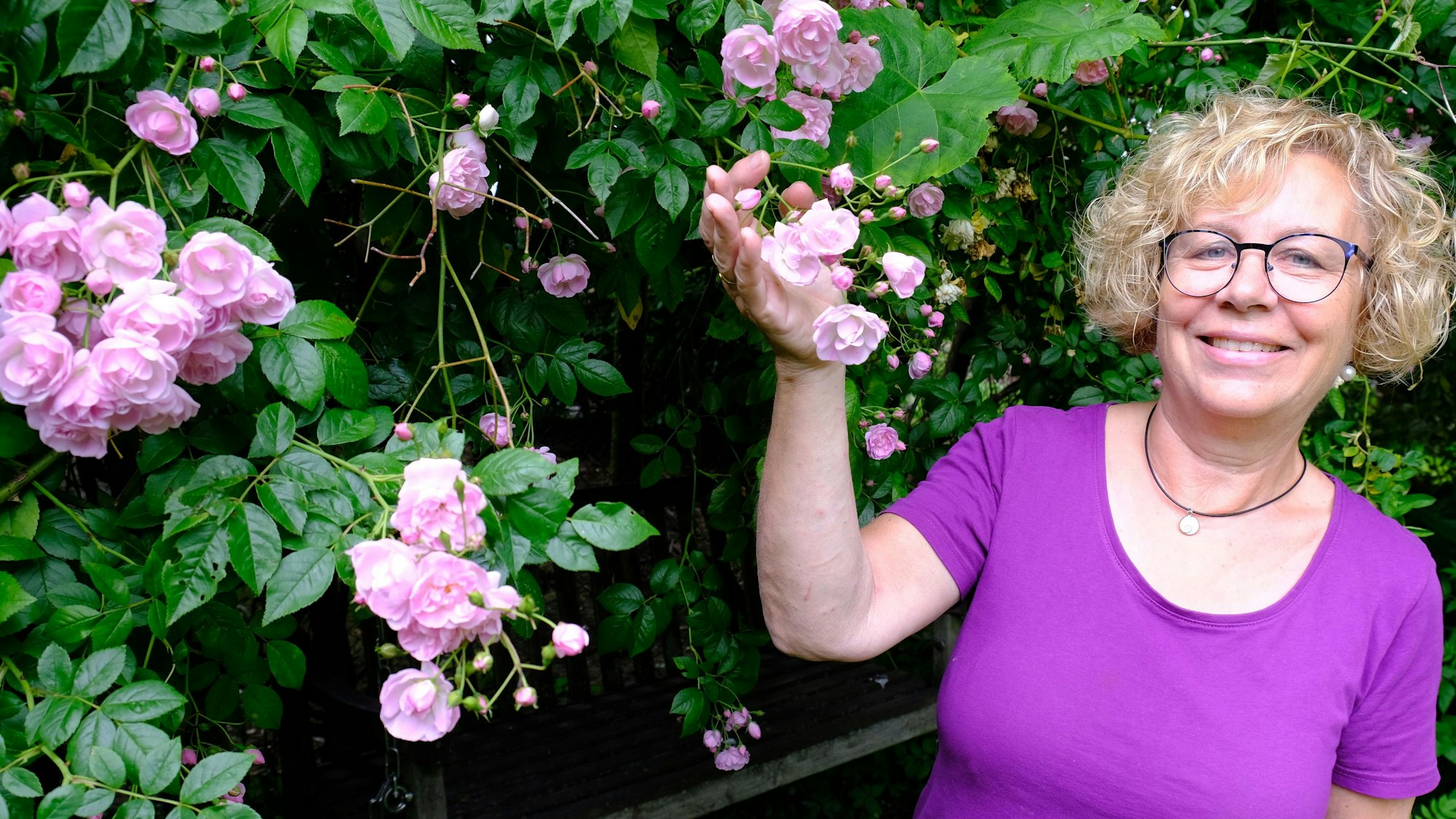Bärbel Geusen steht in ihrem Garten an einer Rose der Sorte Princesse Louise, deren Blüten sie präsentiert.