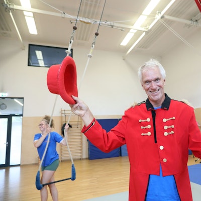 Heiner Kötter, der ehemalige Geschäftsführer vom Kölner Spielecircus, steht in der Übungshalle in Vogelsang, trägt ein Zirkus-Direktor-Kostüm und hält einen Hut in der Hand.
