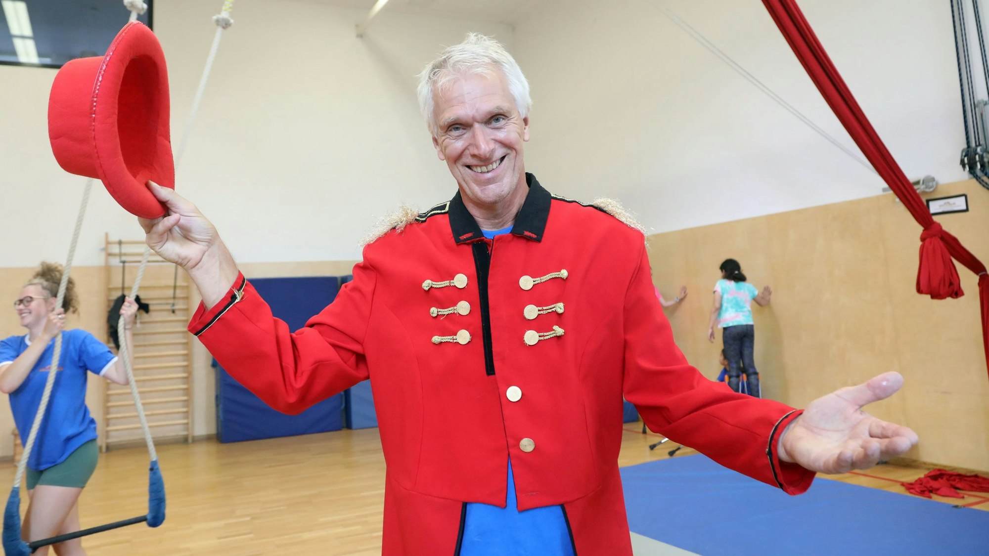 Der Leiter und Mitbegründer des Kölner Spielecircus e.V. steht in der Trainingshalle des Vereins und trägt ein rotes Zirkusdirektor-Kostüm.