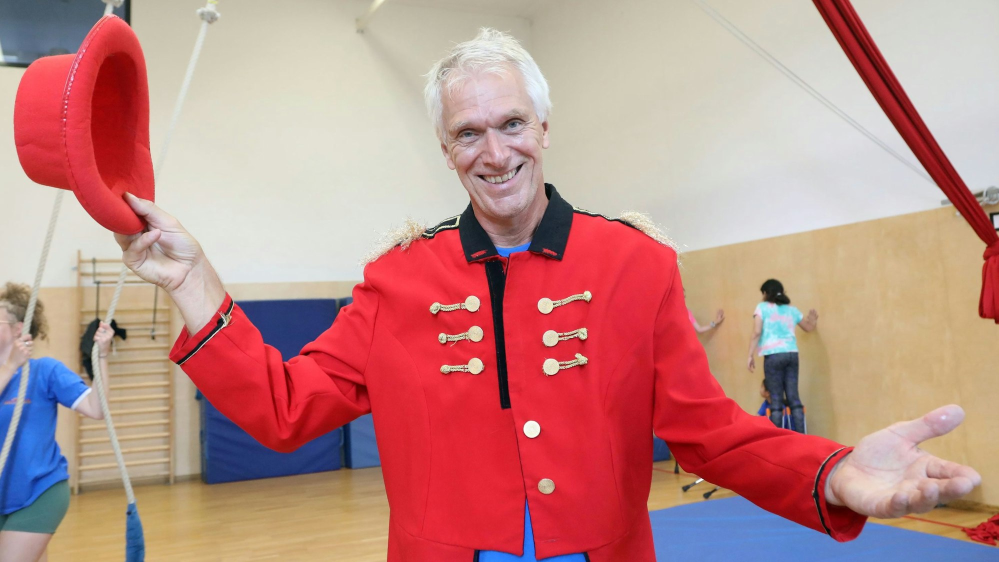 Heiner Kötter, der ehemalige Geschäftsführer vom Kölner Spielecircus, steht in der Übungshalle in Vogelsang, trägt ein Zirkus-Direktor-Kostüm und hält einen Hut in der Hand.