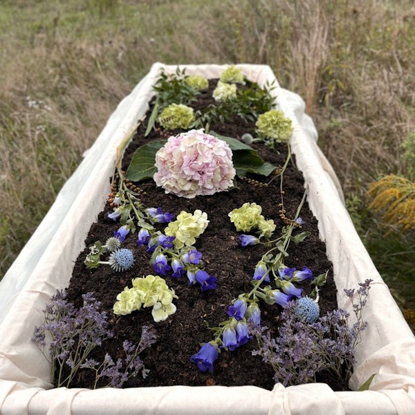 Reerdigung - ein Start-up aus Berlin will in NRW mit einem neuen Beerdigungskonzept Fuß fassen. Zu sehen ist ein offener Sarg mit dunkler Erde gefüllt, auf der Blumen liegen.