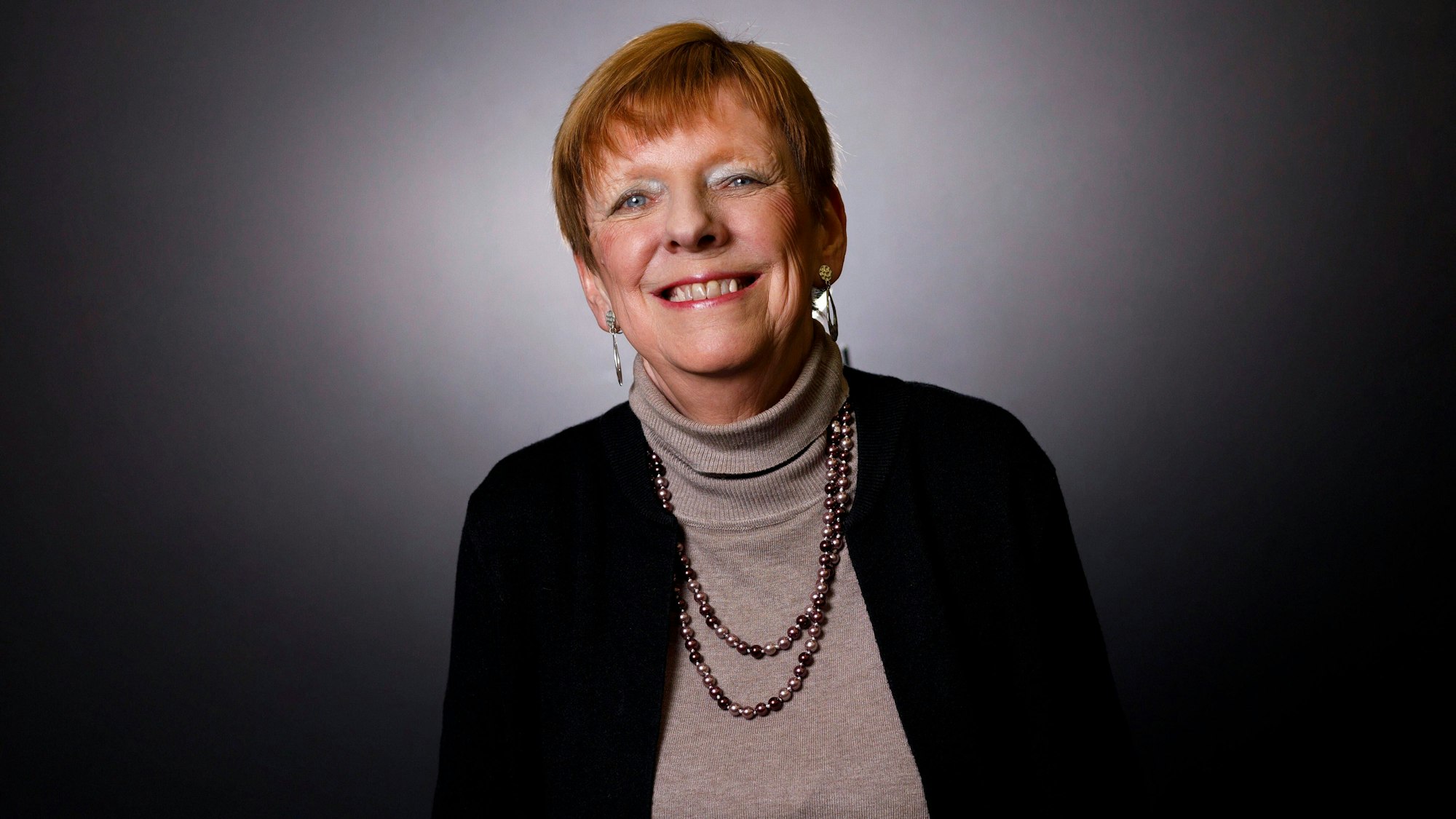 Autorin Eva Weissweiler sitzt bei einem exlusiven Fotoshooting vor einem dunklen Hintergrund.