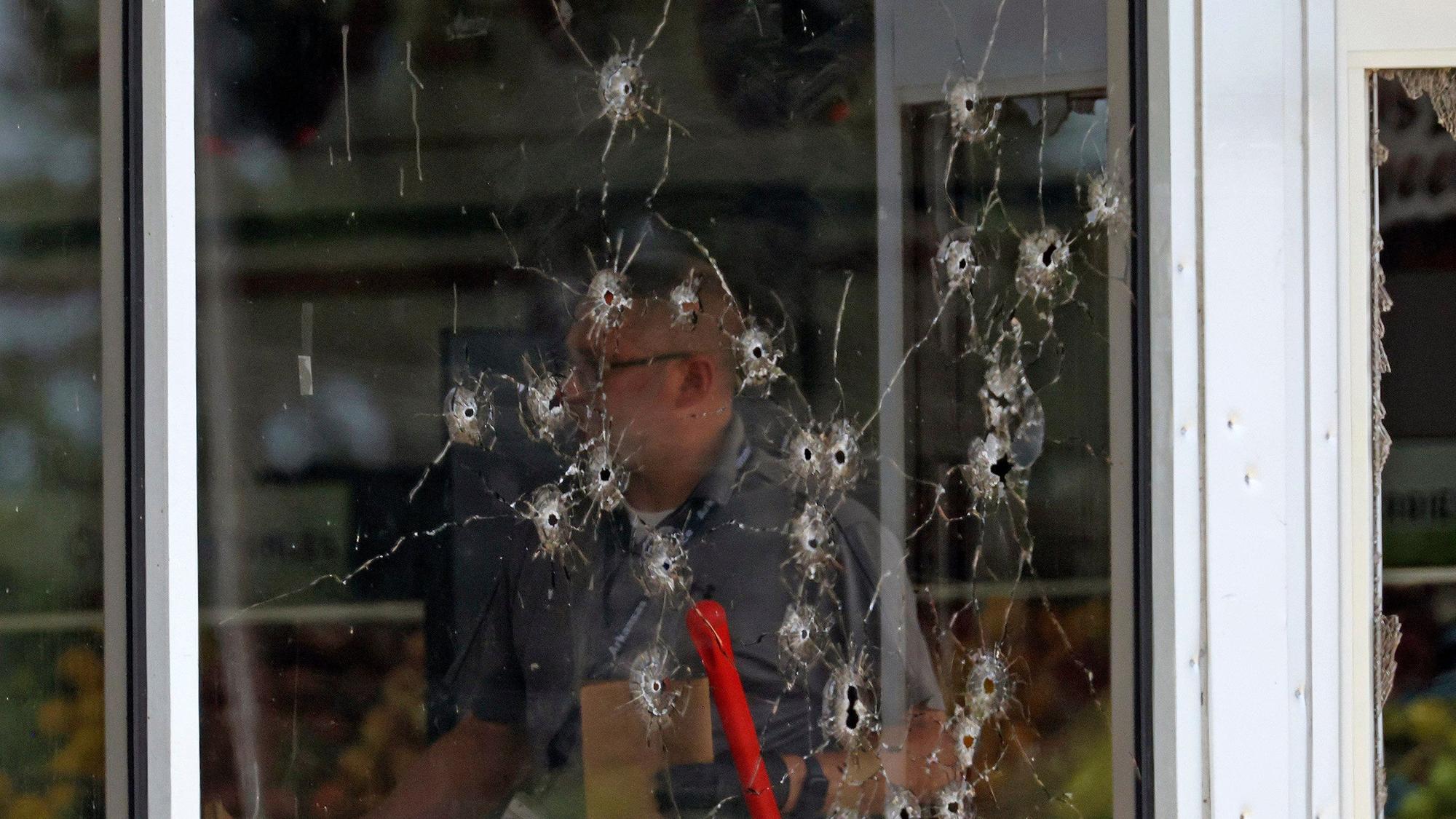 Einschusslöcher sind an einer Fensterfront zu sehen, als Polizeibeamte den Tatort nach Schüssen am «Mad Butcher»-Lebensmittelgeschäft untersuchen.