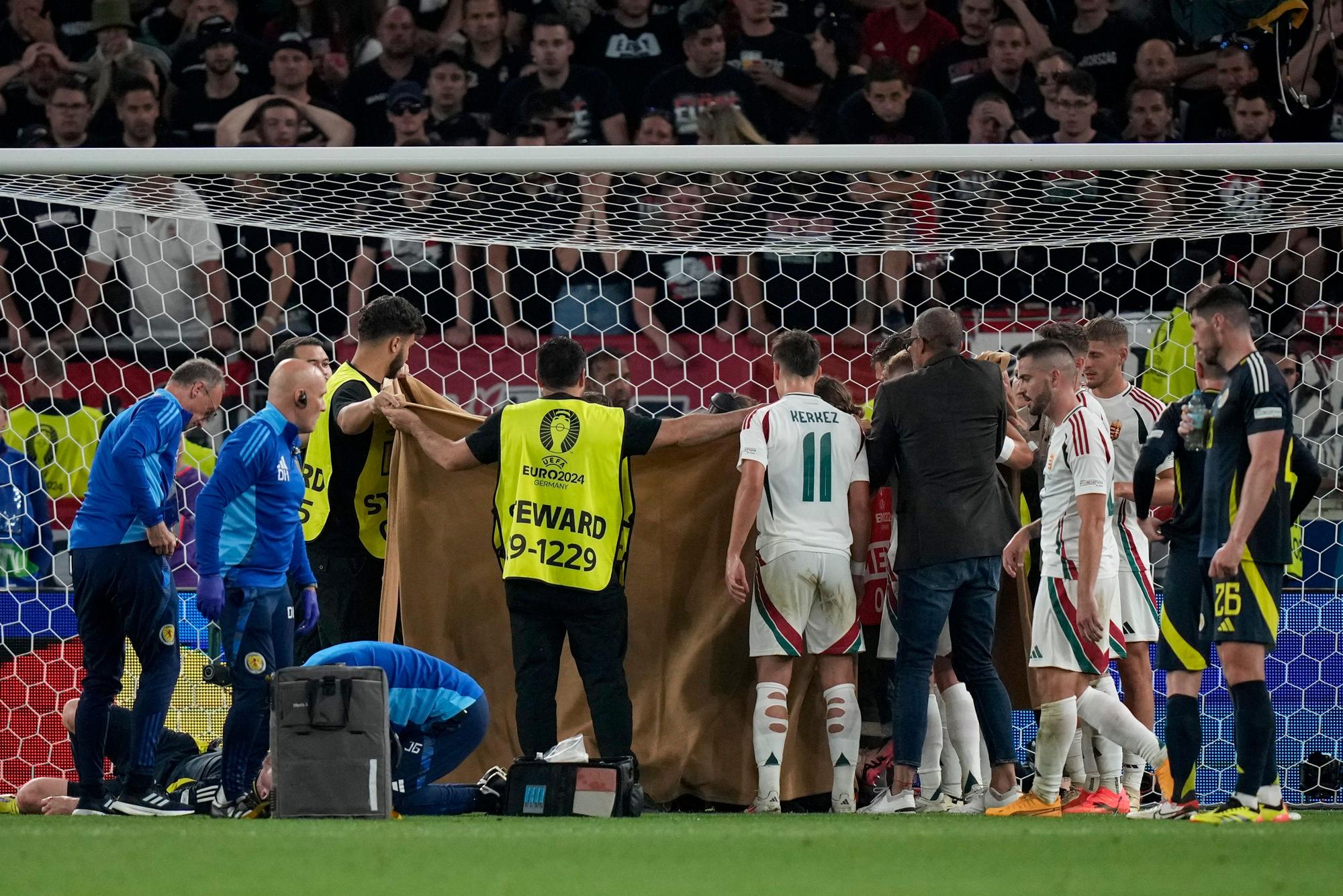 Stewards hold a blanket to protect the privacy of Hungary's Barnabas Varga as he gets medical treatment after a collision during a Group A match between Scotland and Hungary at the Euro 2024 soccer tournament in Stuttgart, Germany, Sunday, June 23, 2024. (AP Photo/Matthias Schrader)