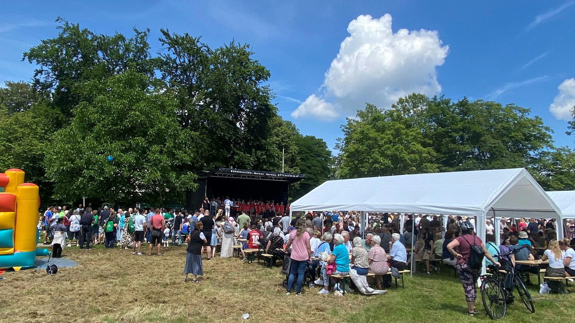 Viele Menschen sitzen bei einer Feier auf einer Wiese.